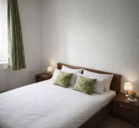 A bedroom in a family house with a double bed, wooden decor flooring, and decorative pillows.