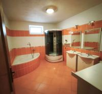 A bathroom in a family house with orange tiles, a bathtub, and a shower corner.