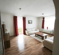 Living room of a family house with a wood-patterned floor, white furniture, and red curtains.