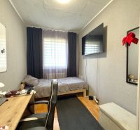 A room in a 4-room apartment with a desk, a bed, and a TV on the wall.
