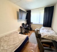 A room in a 4-room apartment with two beds, a wooden decor floor, and a work desk.