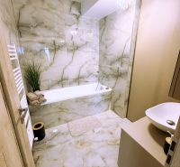 A bathroom with a bathtub, chandelier, and marble tiles in a 2-room apartment.