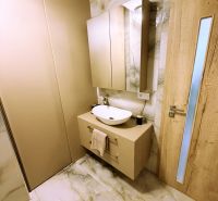 Bathroom with cabinet and sink, marble-patterned tiles, wooden door.