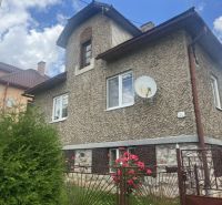 A family house in Rudná with a textured facade, a green fence, and flowers in the garden.