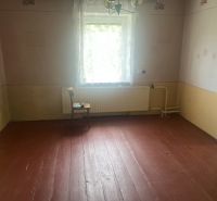 A room in a family house with a wooden floor, pastel-colored walls, a window with a white curtain.