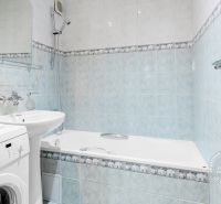 Bathroom with a bathtub, washing machine, and sink in a 2-room apartment with light blue tiles.