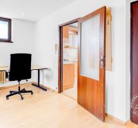 Interior of a 2-room apartment with an office corner, shelf, and door to the kitchen.