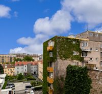 View of buildings and streets of Bratislava with greenery and blue sky.
