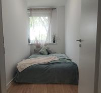 Narrow bedroom with a bed and a window, wooden decor flooring, bright interior.