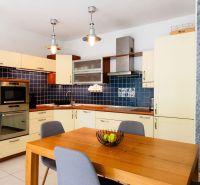 A kitchen in a 2-room apartment with a wooden table, blue tiles, and light cabinets.