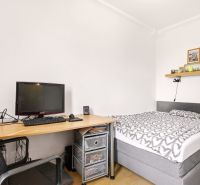 Bedroom in a 2-room apartment with a bed, table, and wooden decor flooring.