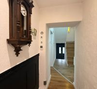 A hallway of a family house with a clock and a wooden decor floor.