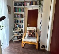 A library in a family house with an armchair, shelves, and a wooden decor floor.