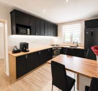 A kitchen in a family house with black cabinets, wooden floor decor, and a large window.