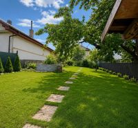 The garden of a family house in Šalgovce with a lawn, trees, and a paved walkway.