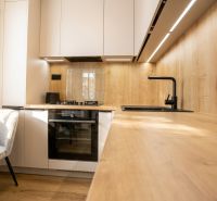 A kitchen in a 2-room apartment with a wooden decor floor, light cabinets, and appliances.