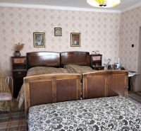 A bedroom in a family house with a wooden bed, patterned wallpaper, and curtains.