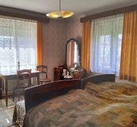 Bedroom in a family house with a bed, table, chairs, and curtains.