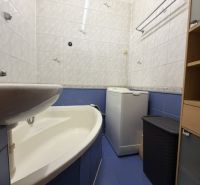 A bathroom in a studio apartment with a bathtub and a washing machine, tiled with white and blue tiles.