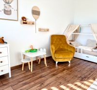 Children's room in a family house with a wooden decor floor, bed, chair, and toys.