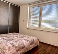 A bedroom in a family house with a large window, a bed, and a floor with a wooden decor.