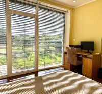 A room in a family house with large windows, blinds, a table, and a computer.