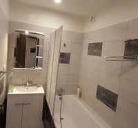 A bathroom with a bathtub and a sink in a 2-room apartment, tiled with light tiles.