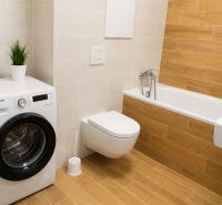 Bathroom with a toilet, bathtub, washing machine, and wooden decor flooring in a studio apartment.