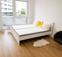 A one-bedroom apartment with a bed, an armchair, a wooden floor, and balcony doors.