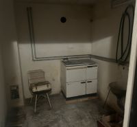 A small room with a kitchen stove, sink, and concrete floor, suitable for a cabin.