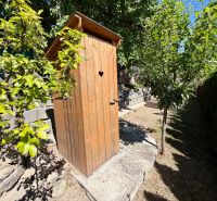 A wooden latrine near a cottage in Kunov, Senica, surrounded by greenery and trees.