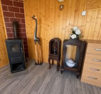 A wooden interior of a cabin with a stove, a giraffe, and furniture on a floor with a wooden decor.