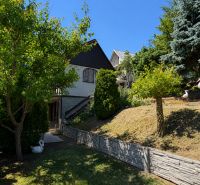 A cottage in Kunov, Senica, surrounded by trees and a garden with stork statues.