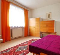 A room in a family house with a light armchair, furniture, and striking orange curtains.