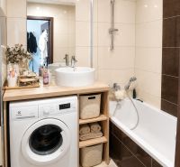 Bathroom in a 2-room apartment with a sink, washing machine, and bathtub, beige tiles.