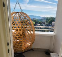 A balcony in a 2-room apartment with a rattan chair and a view of the city.
