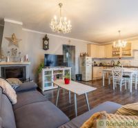 Living room in a family house with a fireplace, kitchen, and wooden decor flooring.