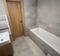 Bathroom in a holiday apartment with a bathtub, sink, and gray tiles.