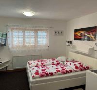 A bedroom in a family house with white walls, a bed, and a television on the wall.