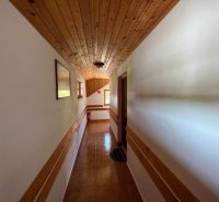 A hallway inside a family house with wooden paneling on the ceiling and walls.