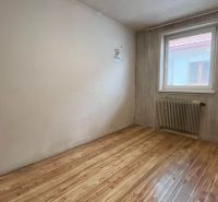 A room with a wooden decor floor, a radiator, and wallpaper in a family house.