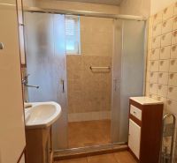 Bathroom in a family house with tiles, a shower corner, and a sink.