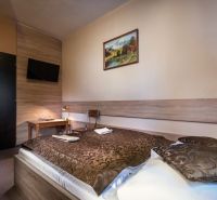 A hotel room interior with a bed, decorative blanket, and a TV on the wall.