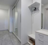 Hallway of a family house with tiles, white furniture, and a large mirror.