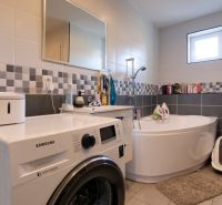 A bathroom in a family house with a corner bathtub and a Samsung washing machine.