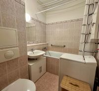A bathroom in a one-room apartment with a bathtub, washing machine, and sink, tiled with tiles.