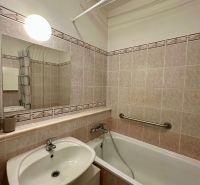 A bathroom in a studio apartment with a bathtub, a sink, and tiles in light shades.