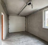 The interior of a garage in a family house with a concrete floor and a white garage door.