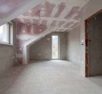 Attic room in a family house with a sloped ceiling, raw walls, and a window.