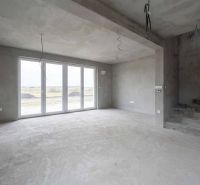 A spacious interior of a family house with large windows and a cement floor.
